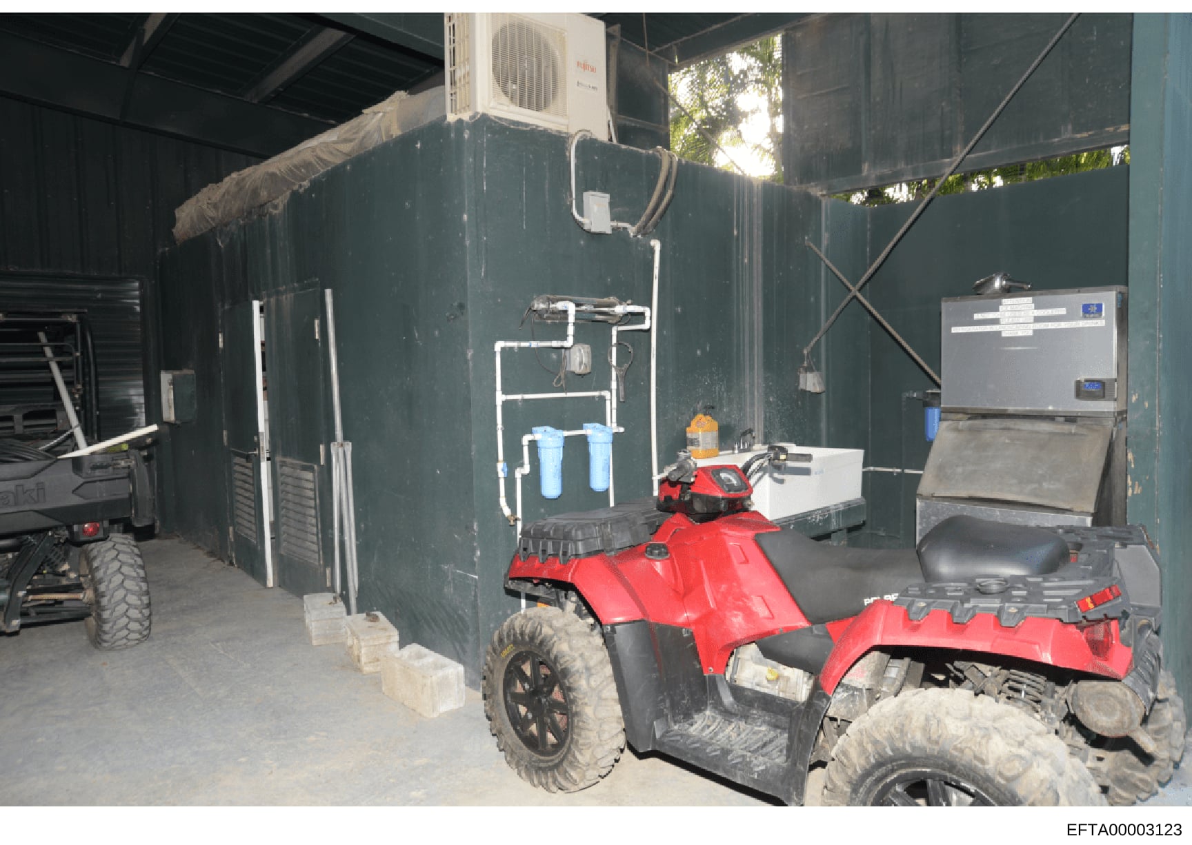 This photograph documents the interior of a utility storage structure containing recreational vehicles (ATVs), water filtration systems, HVAC equipment, and various storage items. The image appears to be evidence documentation from a property search 