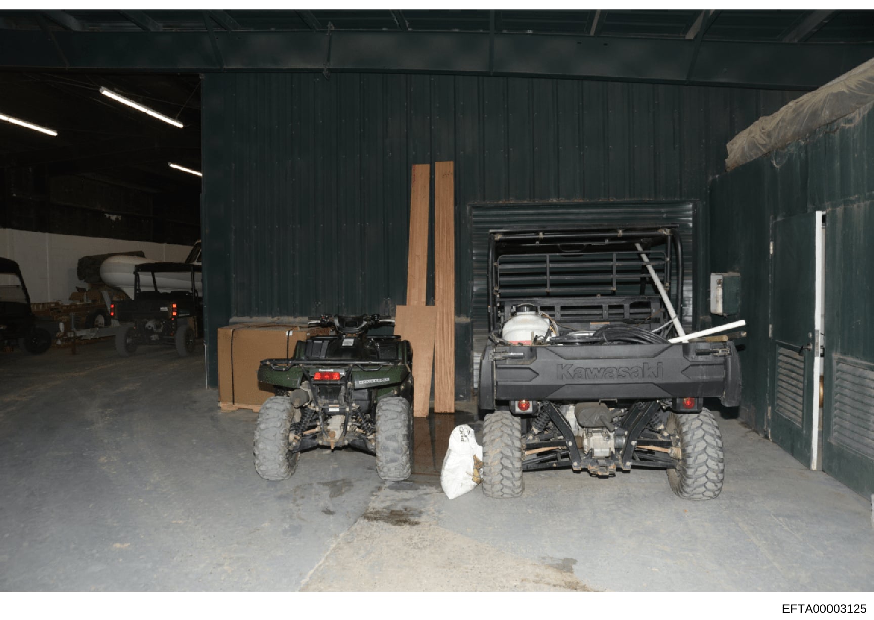 This is a photograph showing the interior of a metal-clad warehouse or storage facility containing multiple all-terrain vehicles (ATVs), including green and black Kawasaki models, along with various tools and equipment. The image appears to be eviden