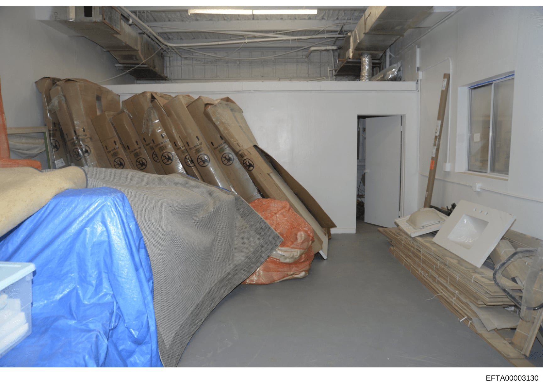 This photograph shows an interior storage or warehouse space containing multiple rolled materials in cardboard tubes, plastic sheeting, and various building or construction materials. The image appears to be documentary evidence from the investigatio