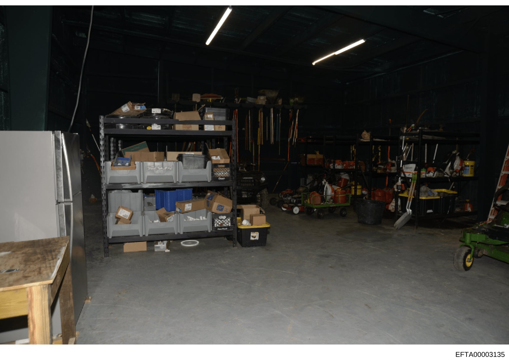 This photograph shows the interior of a storage or maintenance facility, likely connected to one of Epstein's properties. The image documents a garage or warehouse space containing organized shelving units with various boxes and equipment, tools on w