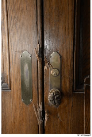 This is a photograph of wooden double doors featuring ornate brass hardware, including a lock mechanism and decorative knob. The doors appear to be part of a property inventory or evidence documentation, showing the architectural details and conditio