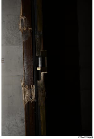 This is an evidence photograph showing a close-up detail of a wooden door frame with visible damage to the wood and what appears to be a brass or metal lock mechanism. The image appears to be from a property inspection or forensic documentation, like