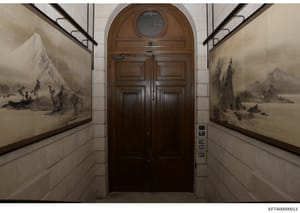 This photograph shows an interior hallway or elevator vestibule in what appears to be a high-end residential or commercial building. The space features elegant architectural details including a dark wood double door with arched transom window, white 