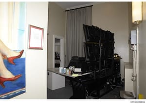 This photograph shows an interior room containing computer equipment, multiple monitors mounted on a wall, and office/workspace furniture. The room appears to be part of a residential property with modern amenities, including curtained windows, artwo
