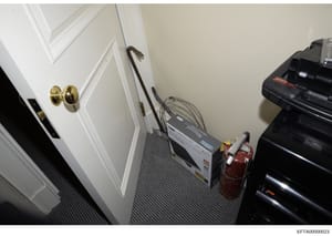 This photograph shows the interior of a closet or utility space, featuring electrical equipment including what appears to be a server or network device with cables, a fire extinguisher, and various household items. The space has white paneled doors w