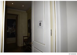 This is a photograph of an interior hallway in what appears to be an upscale residence, showing a white paneled door marked with the letter 'E' and a Bates stamp. The image documents the interior layout of a property, likely taken during an evidence 
