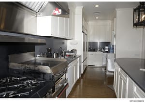 This photograph shows a professional-grade kitchen interior featuring white cabinetry, black granite countertops, commercial cooking equipment including a gas range and hood vent system, and stainless steel appliances. The image appears to be documen