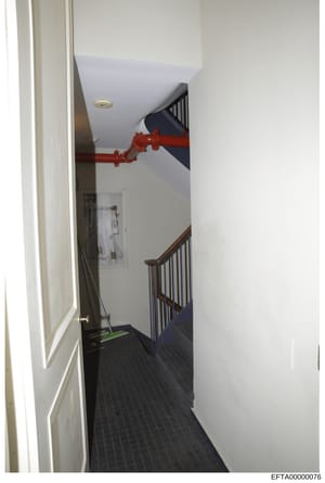 This photograph shows an interior stairwell featuring a multi-level landing with wooden railings and dark flooring. A red fire suppression pipe or sprinkler system is prominently visible running across the ceiling. The image appears to be part of pro
