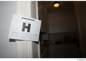 This is an evidence photograph taken during a search warrant execution, showing a doorway or entrance with an evidence scale marker (marked with 'H') affixed to document paper. The photo documents a specific location within a property during the inve