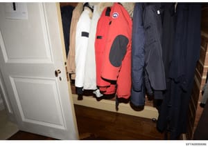 This is an evidence photograph showing the interior of a closet containing multiple winter coats and jackets in various colors including red, white, navy blue, and tan. The red jacket features a circular patch or emblem. The photo appears to be from 