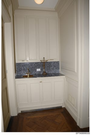 This is an evidence photograph showing a high-end bathroom interior featuring custom white cabinetry, a double sink vanity with dark granite countertop, brass fixtures, and decorative wall paneling. The photo documents the interior design and fixture