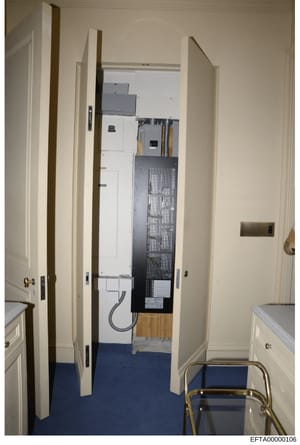 This is an evidence photograph showing the interior of a room containing electrical panels, HVAC equipment, and utility infrastructure. The image appears to be from a property inspection or forensic documentation, featuring white-painted walls, a blu