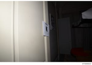 This is an evidence photograph showing an interior room with a white label marker bearing the letter 'K' affixed to a door frame or wall. The photo appears to be taken during a property search or investigation, with the marker used to identify and ca
