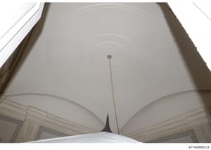 This is a photograph of an interior ceiling featuring classical architectural elements including a domed or barrel-vaulted ceiling with concentric circular details, decorative molding, and ornamental borders on the walls. The image appears to be take