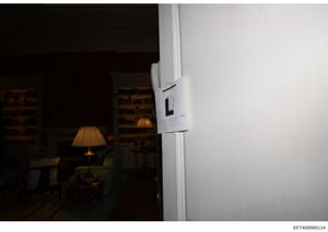 This is a photograph of an interior room, likely from one of Jeffrey Epstein's residences, showing a living space with furniture, lighting fixtures, and bookshelves in the background. A white evidence documentation label is visible on the right side 