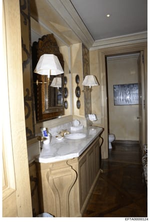 This is a photograph of an upscale bathroom interior, likely from one of Jeffrey Epstein's properties. The image shows a marble vanity with dual sinks, ornate framed mirrors with decorative sconces, high-end finishes, and access to an adjacent room w