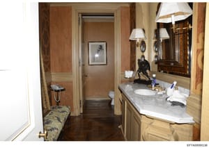 This is a photograph of an upscale residential bathroom featuring marble countertops, wood cabinetry, dual sconces, and decorative elements. The image appears to be documentation of property interiors, likely from one of Jeffrey Epstein's residences,