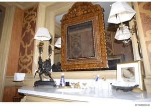 This is a photograph of an upscale bathroom interior featuring an ornate wooden-framed mirror, elegant vanity counter with marble or stone surface, decorative lighting fixtures, and luxury furnishings. The image documents the interior design and déco