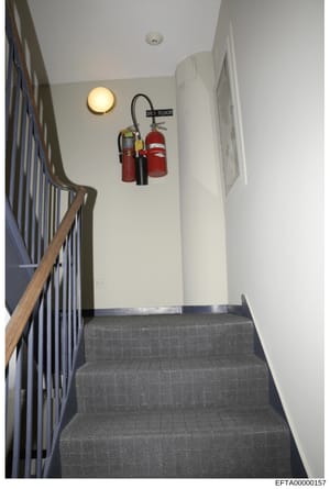 This is an evidence photograph showing the interior of a stairwell landing on the third floor of a building, featuring fire extinguishers and safety equipment mounted on the wall. The image documents the physical layout and safety infrastructure of w