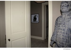 This is a photograph of an interior hallway in what appears to be a residential property, showing white-trimmed doorways, a gray accent wall with framed artwork, and a decorative blue and white ceramic or porcelain figure visible on the right side. T