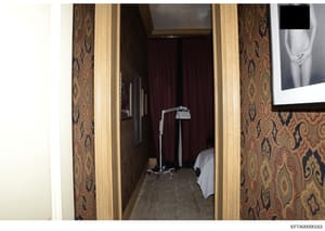 This is an evidence photograph showing the interior of a residential room with decorative damask-patterned wallpaper in gold and burgundy tones. The image captures a doorway entrance with cream-colored molding, revealing a carpeted floor, a bed with 