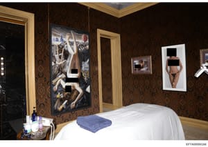 This is a photograph of an interior bedroom space, likely from one of Jeffrey Epstein's residences, showing ornate wallpaper, framed artwork on walls, a massage table with white linens, and personal care items on a side table. The room contains multi