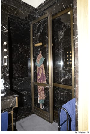 This evidence photograph shows a high-end bathroom interior featuring black marble walls with gold/brass fixtures and hardware. A garment (purple and patterned dress or robe with teal/green collar or wrap) is displayed on a hanger within a recessed n
