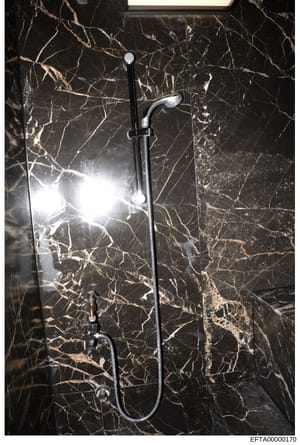 This is a photograph of a luxury bathroom shower installation, showing a contemporary chrome showerhead and handheld shower fixture mounted on black marble veined walls. The image appears to be evidence documentation from a property associated with t