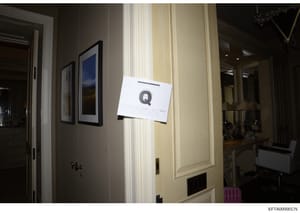 This is an evidence photograph showing the interior of a room with a white evidence marker labeled 'Q' affixed to a wall. The photo documents the location and condition of an item or area of interest during the investigation. The room features contem