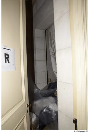 This is an evidence photograph showing an interior room or closet space with what appears to be furniture covered in dark plastic sheeting. An evidence marker labeled 'R' is visible on the wall, indicating this photo was taken during a forensic inves