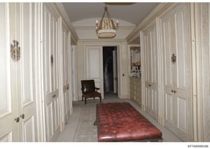 This is a photograph of a luxurious residential hallway featuring cream-colored paneled doors, a brass chandelier, ornate molding, and high-end furnishings. The image appears to be documentation of an interior space from one of Epstein's properties, 