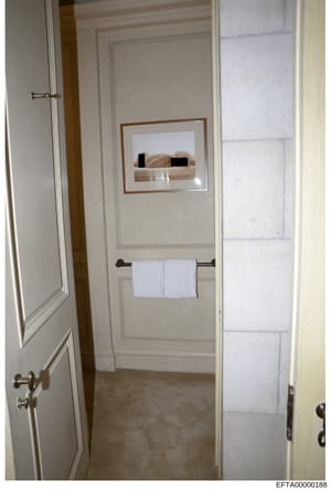 This is an evidence photograph of a bathroom interior, showing a framed artwork with censored/redacted figures, a towel rack with folded white towels, and white paneled walls. The image appears to be from a property inspection or evidence documentati