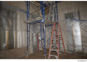 This photograph documents an interior space under construction or renovation, showing temporary blue metal scaffolding, a red ladder, and plastic sheeting used for dust and debris containment. The image appears to be evidence documentation from an Ep