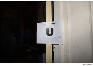 This is a photograph of an evidence marker (marked with 'U') placed on what appears to be an interior wall or surface during a search operation. The marker has a documentation form attached with fields for search personnel name, agency, contact numbe