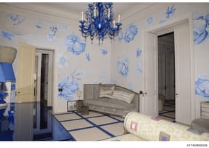 This is an architectural or interior design rendering showing a luxuriously decorated room with blue-and-white botanical wallpaper, ornate blue Murano glass chandelier, gray upholstered seating, geometric patterned flooring, and multiple doorways. Th