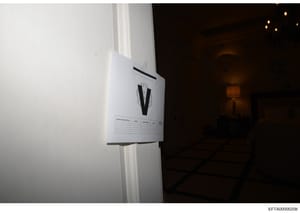 This photograph shows an evidence marker labeled 'V' attached to a white door frame or wall in what appears to be an interior room. The marker contains a data collection table below the letter designation. This type of photo is standard in forensic i