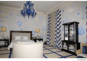 This is a photograph of an elegantly designed bedroom featuring luxury furnishings and decorative elements. The room displays a sophisticated color scheme of blue and white with high-end finishes, including a distinctive round bed, ornate chandelier,