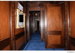 This photograph shows a formal hallway inside one of Jeffrey Epstein's residences, featuring high-end wood paneling, inlaid decorative details, blue carpeting, and ornate furnishings. The image appears to be evidence documentation from the investigat