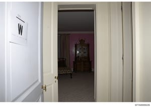 This is an evidence photograph showing an interior view through an open doorway into a residential room. The image captures a doorway with brass hardware on the left, leading into a room with burgundy/wine-colored walls, decorative antique furniture 