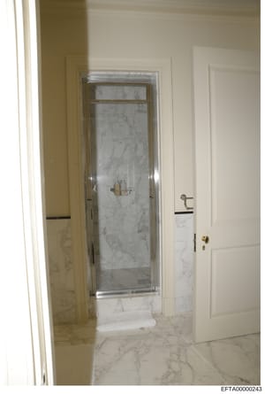 This photograph shows a luxury bathroom interior featuring white marble walls and flooring, a glass-enclosed shower stall with chrome fixtures, and white painted doors with brass hardware. The image appears to be from a property inspection or invento