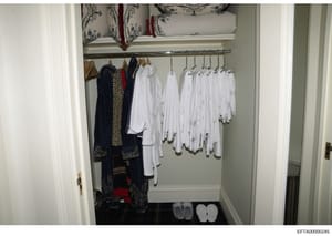 This photograph shows the interior of a closet or dressing room, displaying an organized collection of clothing including formal wear, white garments, and decorative items. The image appears to be evidence documentation from the Epstein investigation