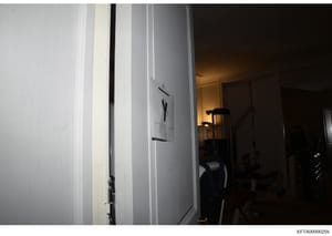 This is an evidence photograph taken during an investigation, showing an interior hallway or passage area with white walls, doorways, and minimal furnishings. The image appears to be part of a property search or documentation of a residential or comm