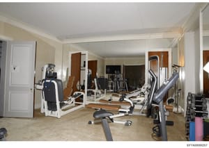 This photograph documents a luxurious private home gymnasium featuring multiple professional-grade exercise machines, weights, and fitness equipment. The room displays extensive wall-to-wall mirroring, polished flooring, and high-end finishes. The sp