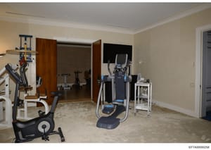 This photograph shows an upscale, professionally equipped private gym or fitness room within a residence. The space contains multiple pieces of exercise equipment including stationary bikes, elliptical machines, and weight training apparatus. The roo