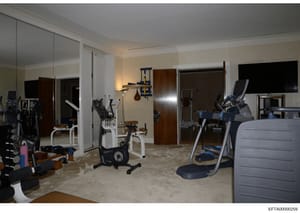 This photograph shows a professionally equipped home gym space within what appears to be a luxury residence. The room contains multiple exercise machines including stationary bikes, elliptical equipment, and weight training apparatus, along with mirr
