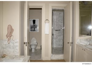 This photograph documents the interior of a luxury bathroom featuring marble countertops, vanities, a toilet, shower enclosure, and wall-mounted artwork. The image appears to be part of property documentation, possibly related to one of Epstein's res