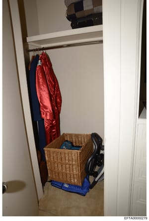 This is an evidence photograph showing the interior of a closet space, likely from one of Epstein's properties. The image depicts a narrow closet with hanging clothes (including a red jacket and dark blue garment), a wicker storage basket, exercise e