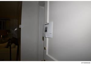 This is a photograph of an interior doorway with a white frame and brass door hardware. An evidence tag or documentation label is affixed to the door frame, suggesting this photo was taken during an investigative search or forensic documentation of a