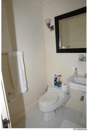 This is a photograph of a residential bathroom showing standard fixtures and layout. The image documents a clean, modest bathroom with white ceramic fixtures, a single vanity sink with mirror, toilet, and towel rack. The photo appears to be evidence 