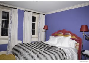 This is a photograph of a residential bedroom interior, featuring bold purple walls, a red ornate headboard, white linens, and coordinating furnishings. The image appears to be documentation of interior design or property contents, likely taken as pa
